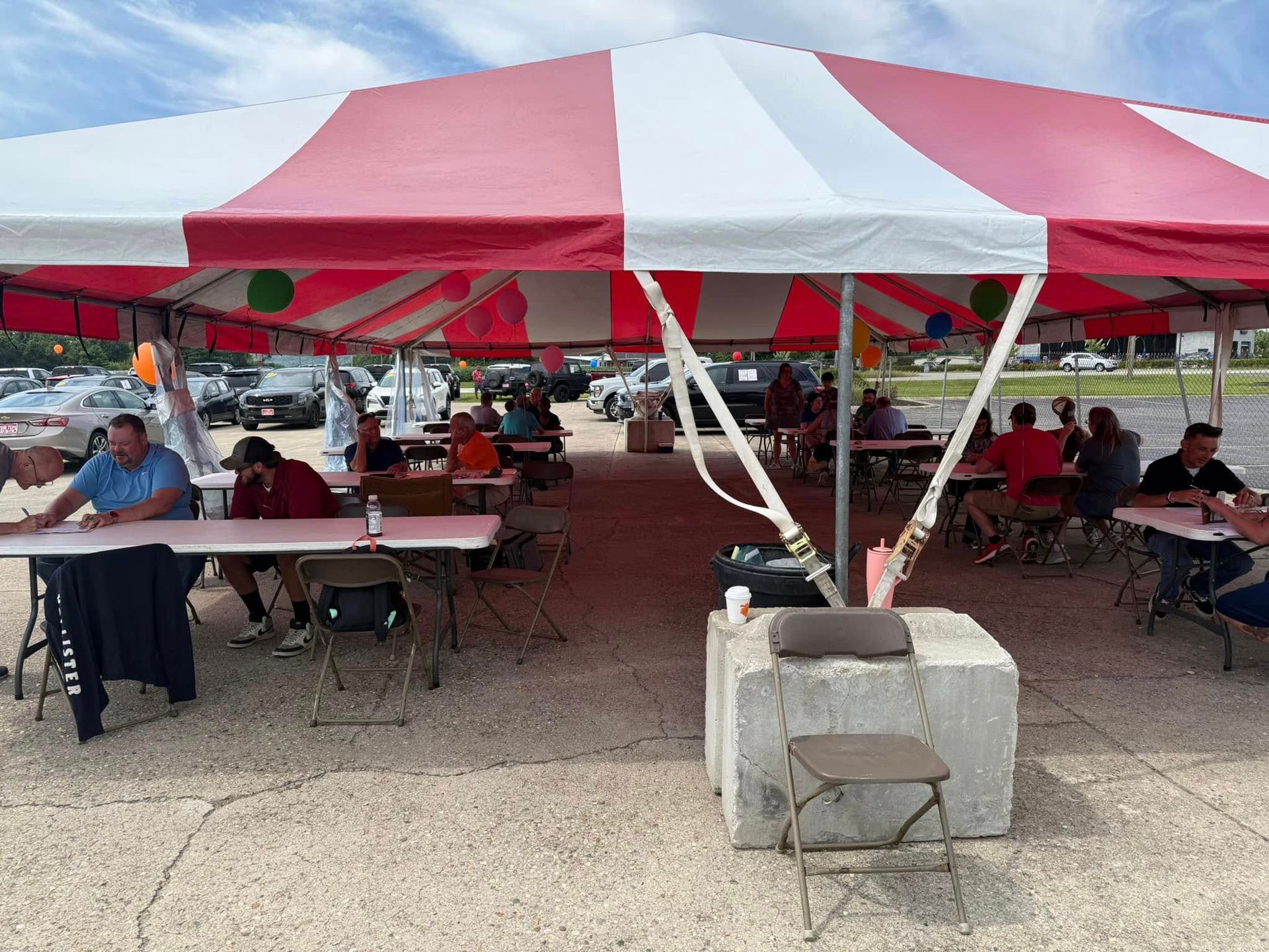 People seated at tables under a red-and-white tent at an outdoor event