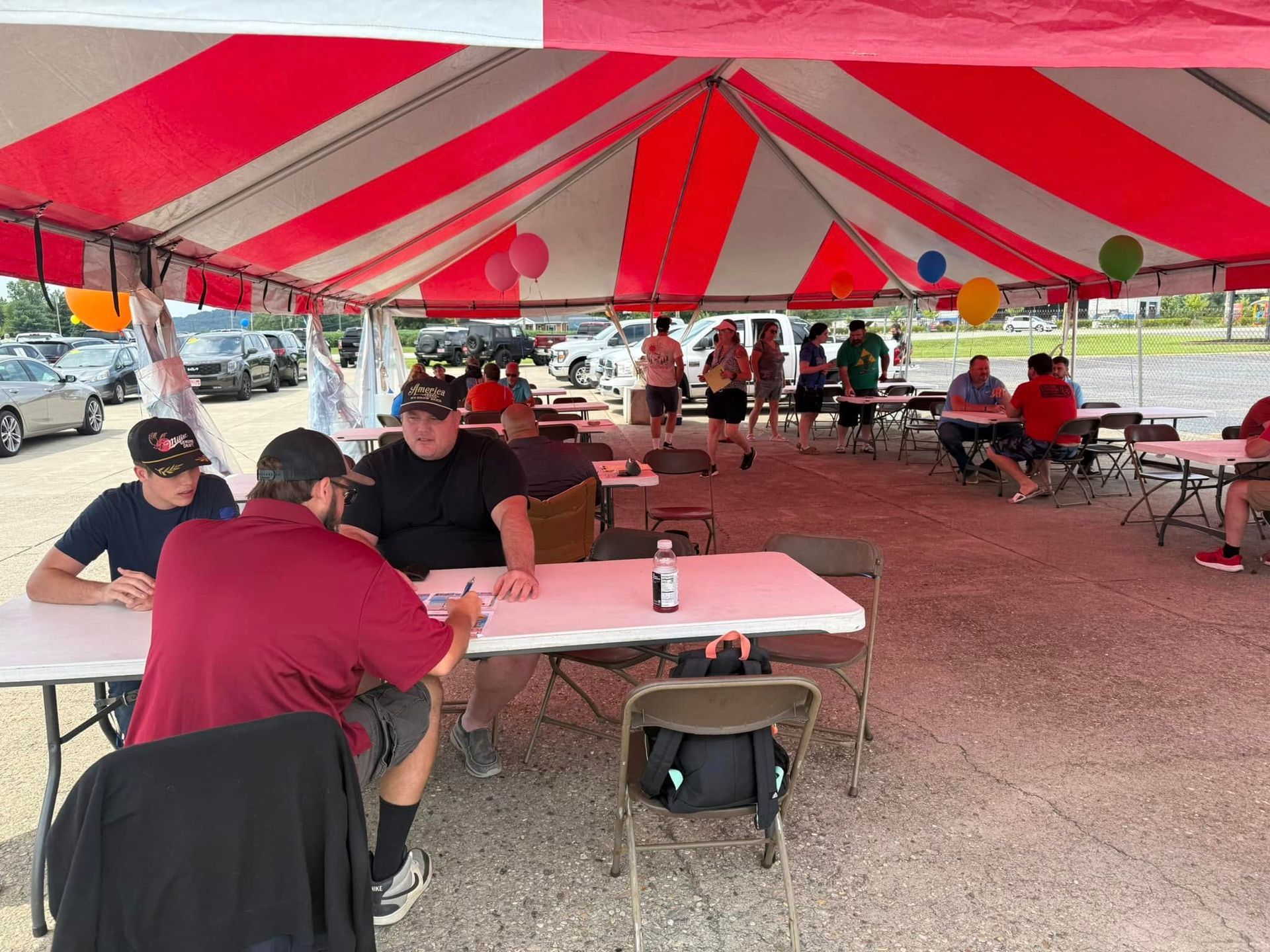 People seated at tables under a red-and-white striped tent at an outdoor gathering