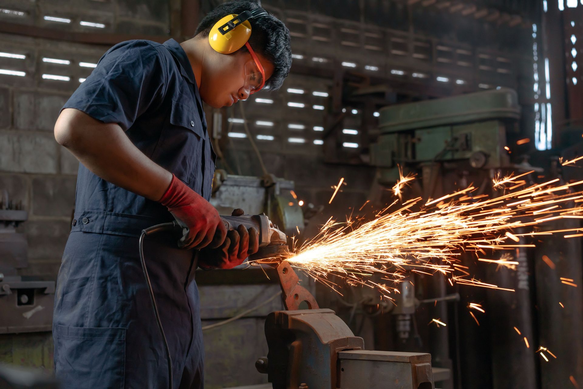A man is grinding a piece of metal in a factory.