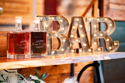 Bar sign with illuminated letters beside two amber liquor bottles on a wooden shelf.