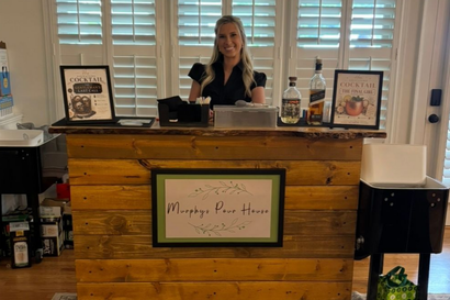 Bartender pouring a cocktail into a margarita glass beside a jigger on a wooden bar