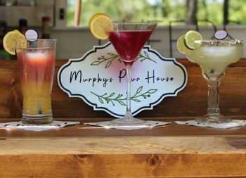 Three colorful cocktails on a wooden table beside a “Murphy’s Pour House” sign