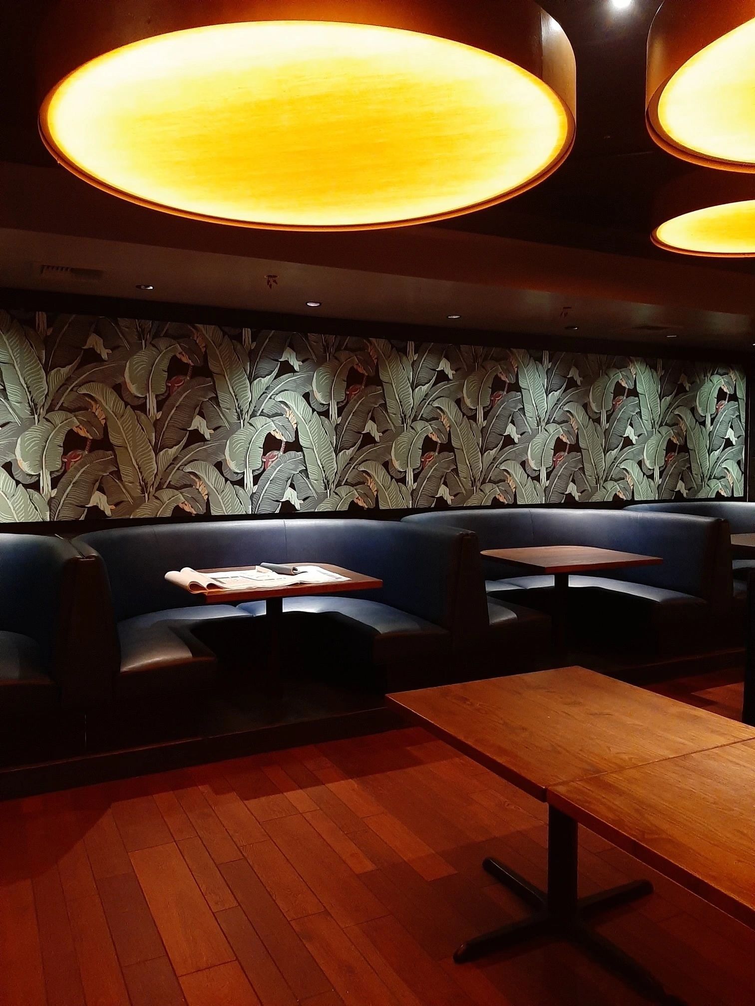 A restaurant with tables and benches and a wall with leaves on it