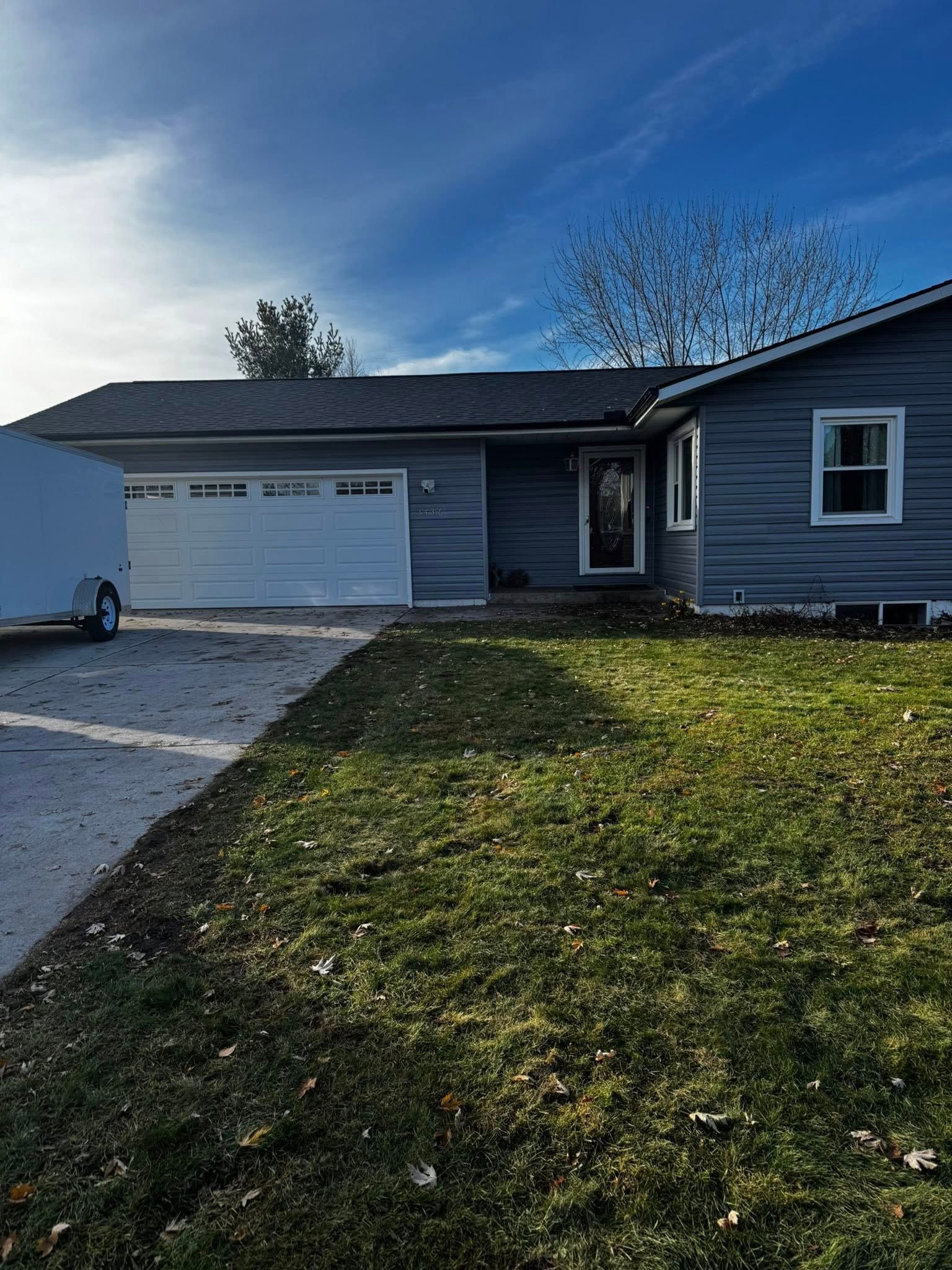 A gray house with a white garage door and a green front lawn under a bright blue sky.