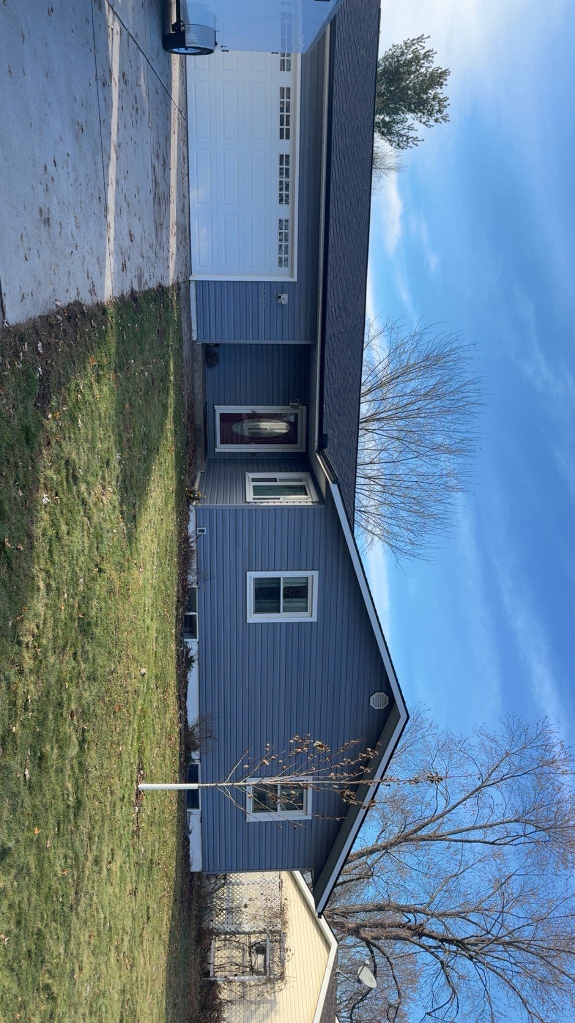 A gray, single-story house with a white garage door, a prominent front door, and visible windows under a bright blue sky.