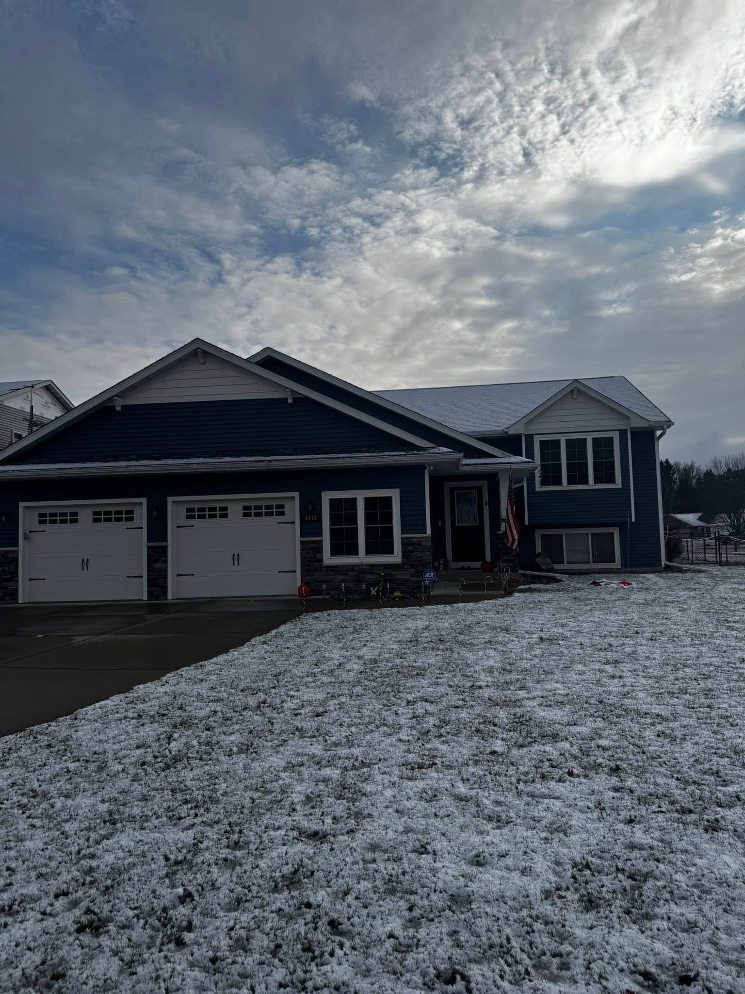 A dark blue, multi-level house with a two-car garage and snow-dusted lawn under a cloudy, bright sky.