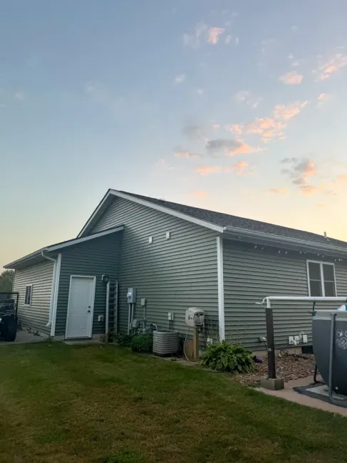 A side view of a green-sided house at dusk with a white door, an outdoor AC unit, and a portion of a swimming pool visible.