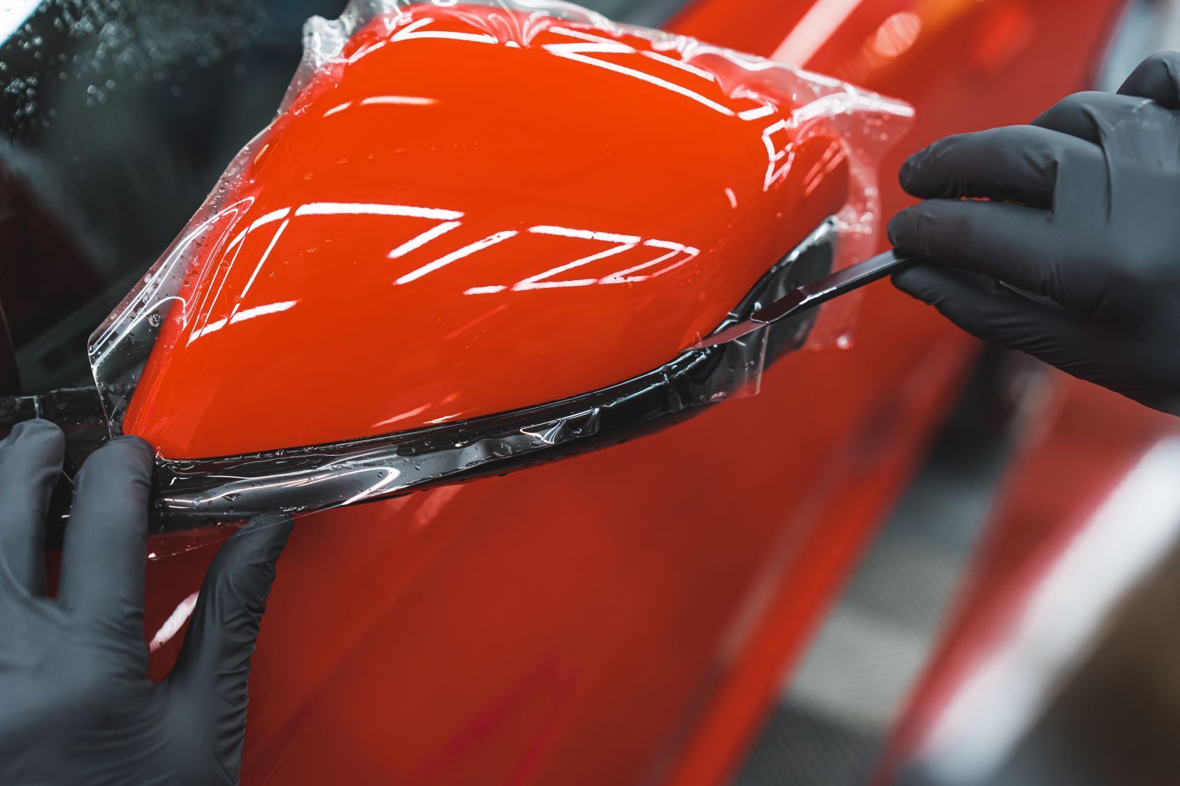 A Person is Wrapping a Red Car With Plastic Wrap — About Town Windscreen Repairs & Replacements in Wulguru, QLD