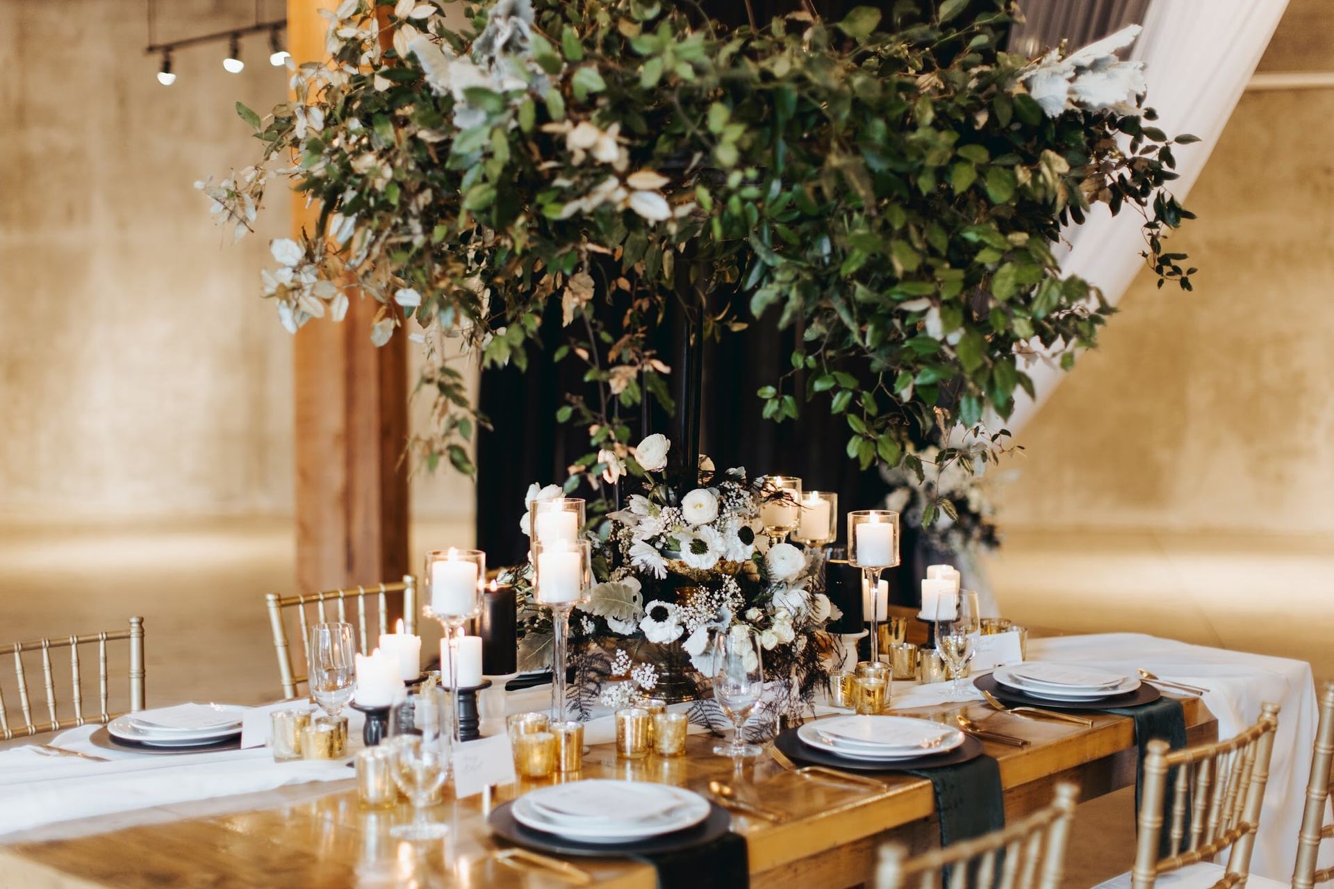 A table set for a wedding reception with plates , candles , and a tree in the middle.