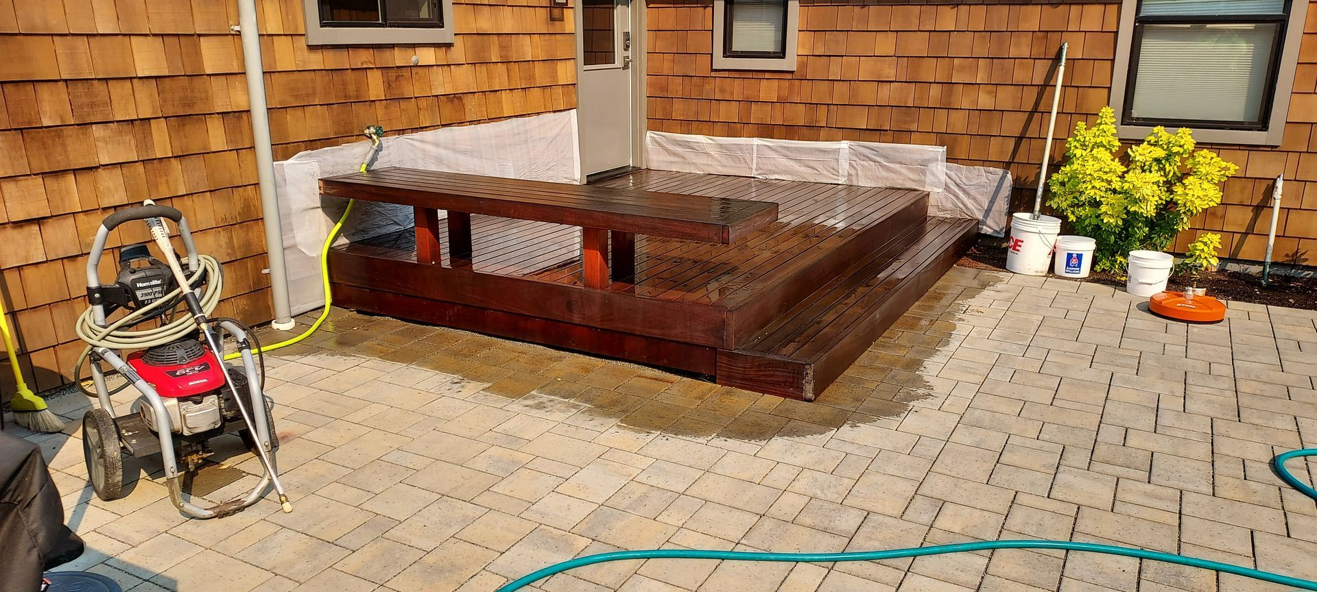 Wooden deck with steps, patio, power washer, and plants.