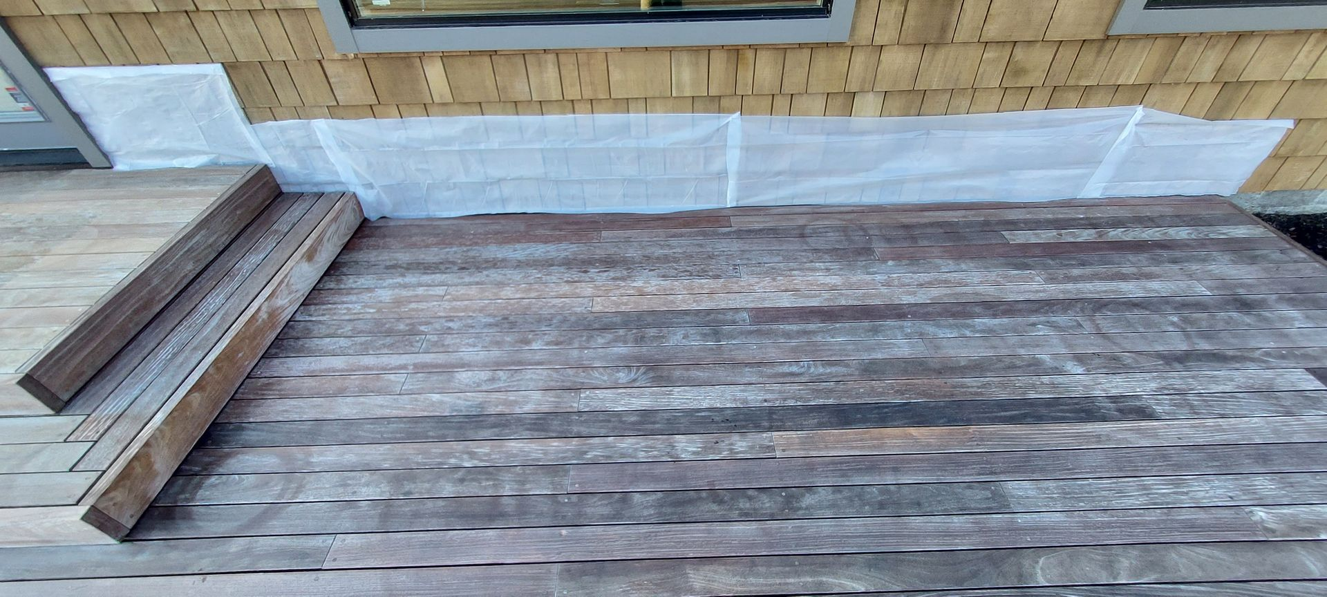 Wooden deck with steps next to a building with light brown siding and a window.