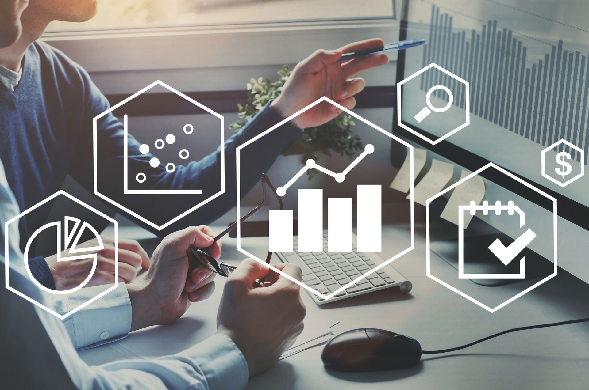 White science and business icons overlaid on an image of business people reviewing charts on a computer at a desk