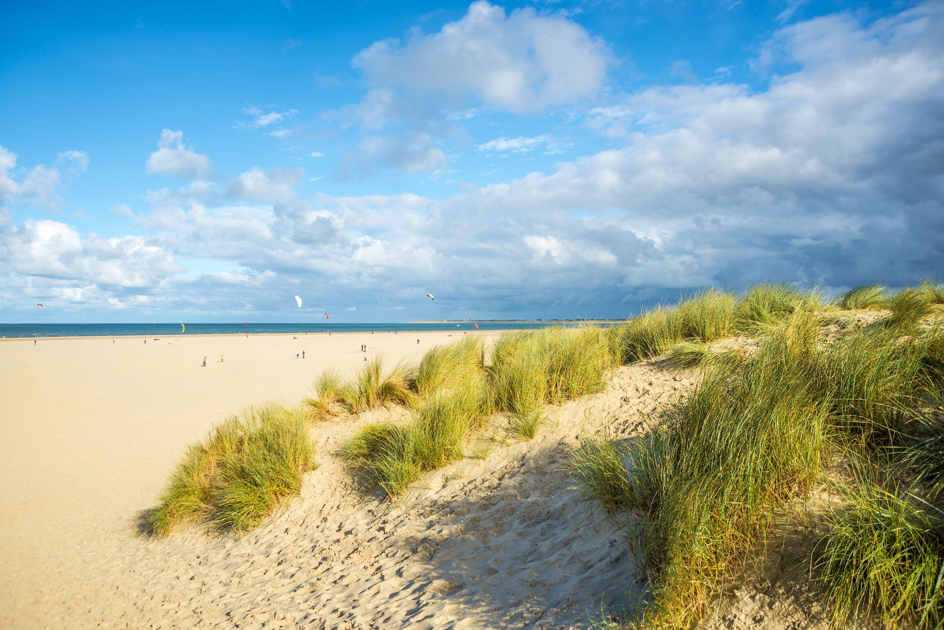 Sonniger Sandstrand mit grasbewachsenen Dünen, blauem Meer und teilweise bewölktem Himmel