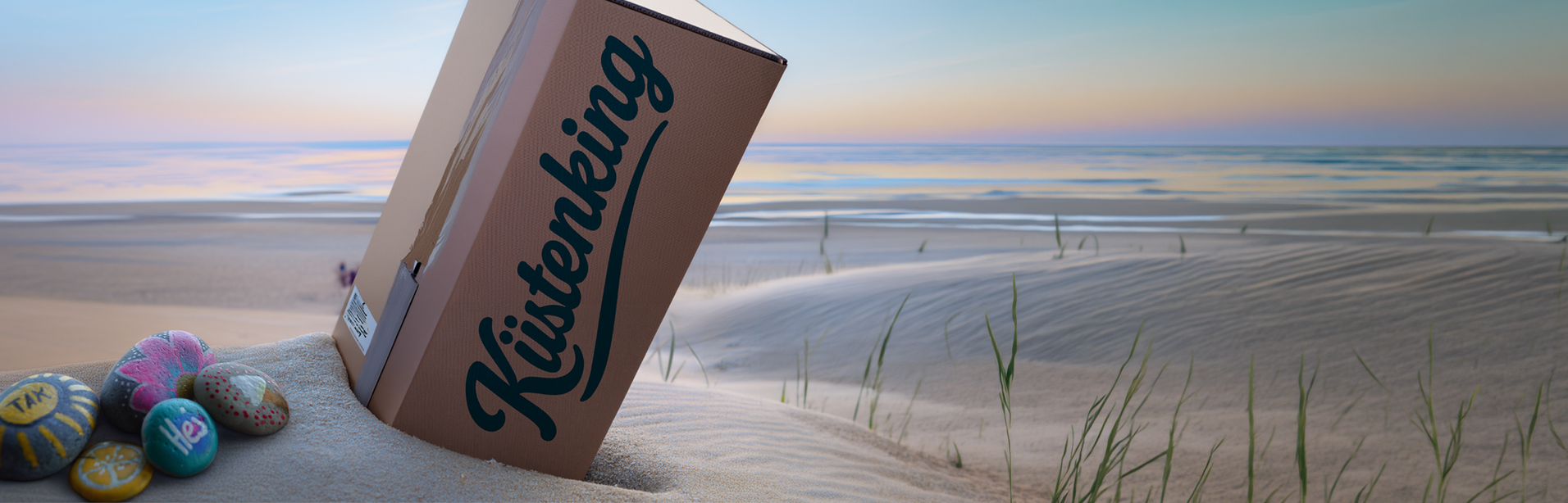 Strandszene mit einem schief stehenden rosa „Finishing“-Schild und bunt bemalten Steinen bei Sonnenaufgang.