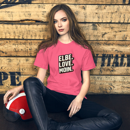 Eine Frau in einem rosa T-Shirt und einer schwarzen Hose sitzt an einer Holzwand; neben ihr steht ein roter Helm.