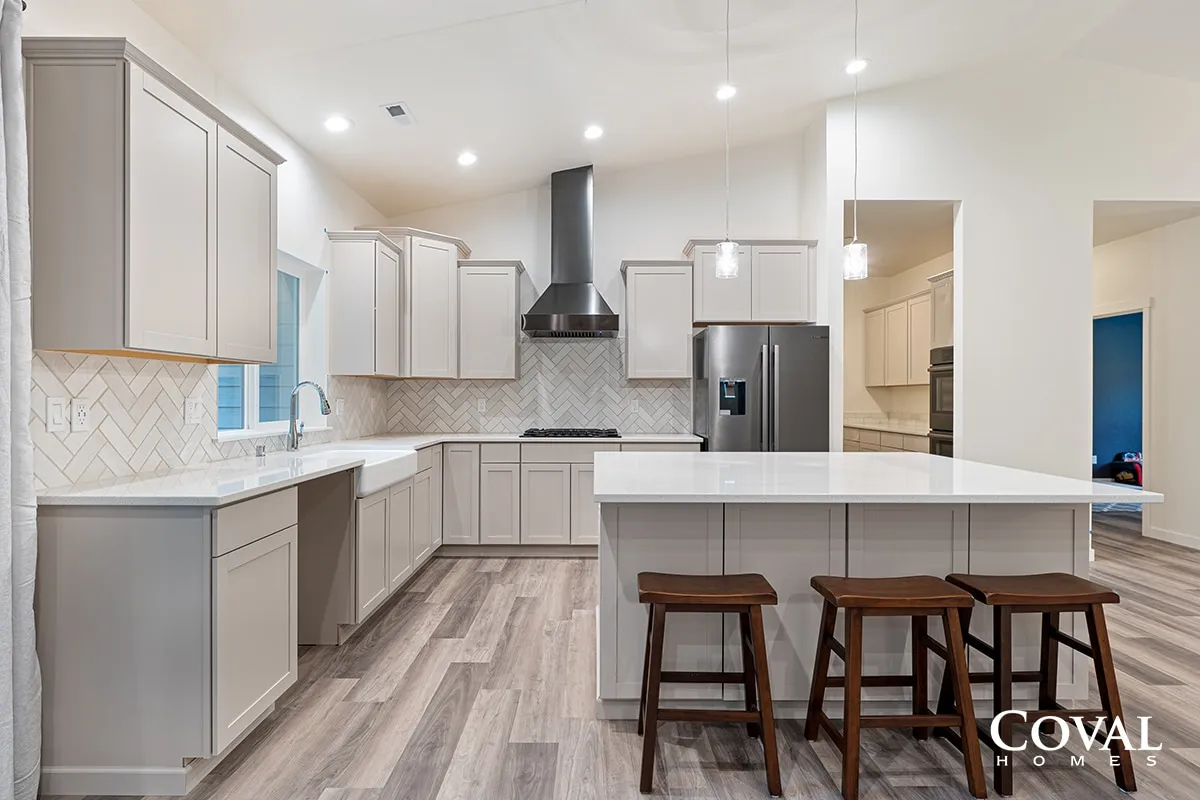 Bright modern kitchen with gray cabinets, white island, stainless appliances, and wood bar stools