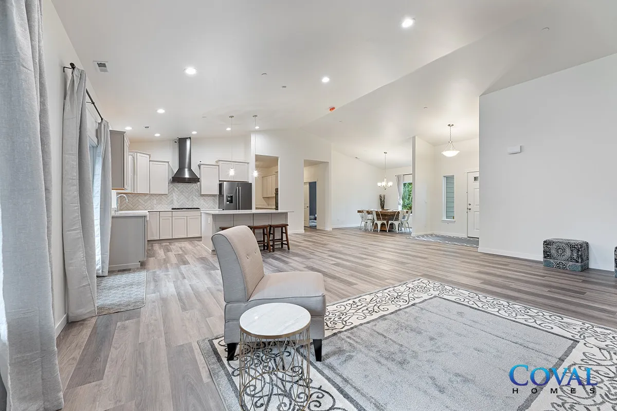 Bright open living room with kitchen, gray chair, rug, and large windows on wood floors