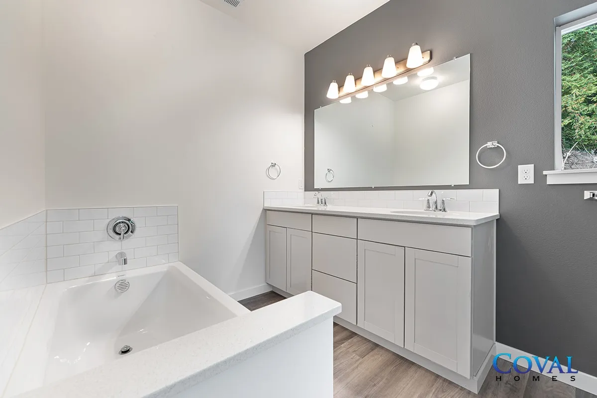 Bright modern bathroom with white tub, gray vanity, large mirror, and pendant lights