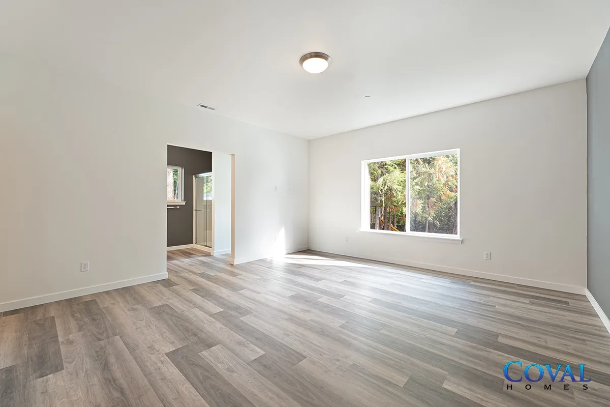 Empty bright room with gray wood flooring, white walls, and a window looking outside