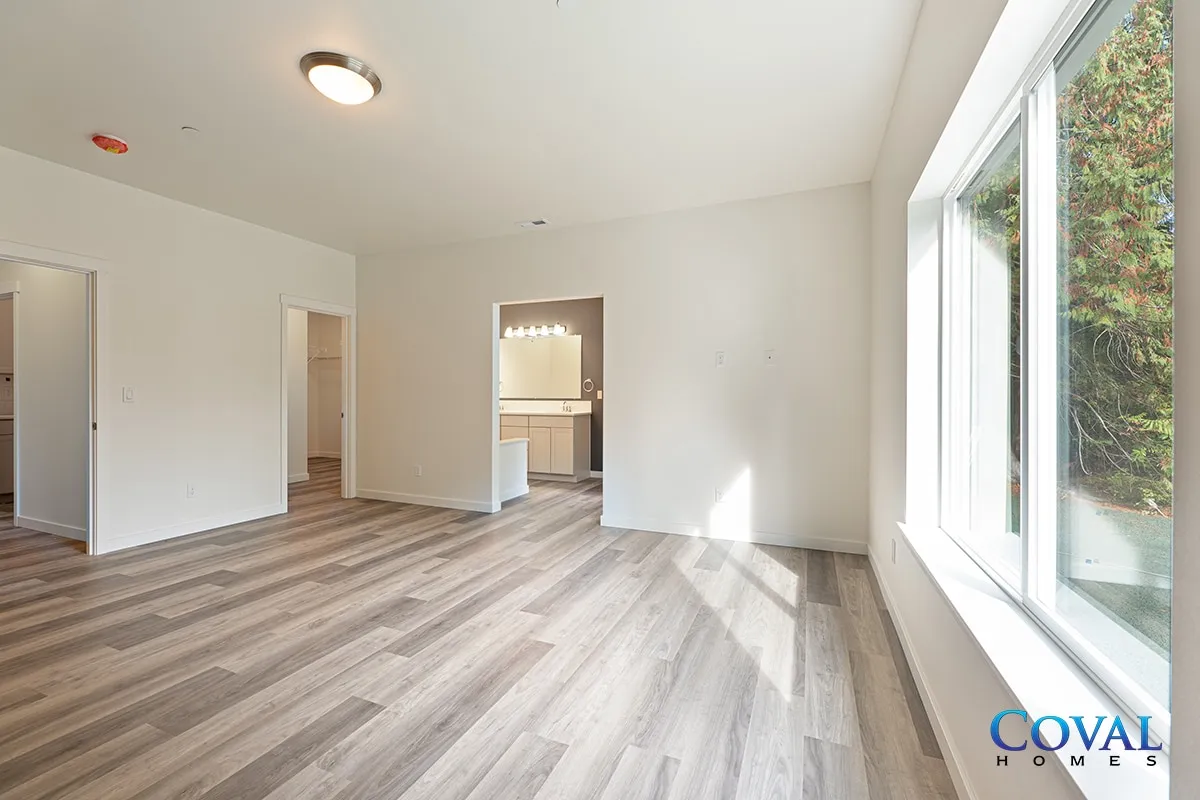 Empty bright living room with wood flooring, white walls, and large sunlit windows