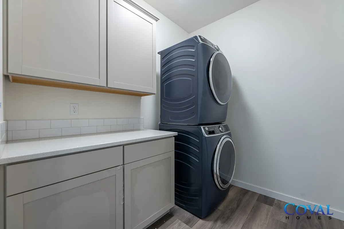 Laundry room with stacked dark blue washer and dryer beside white cabinets and countertop