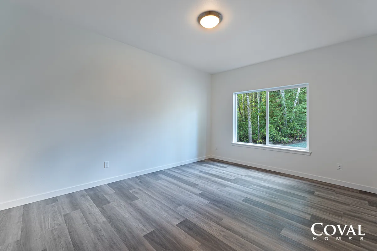 Empty white room with gray wood floors and a window overlooking trees