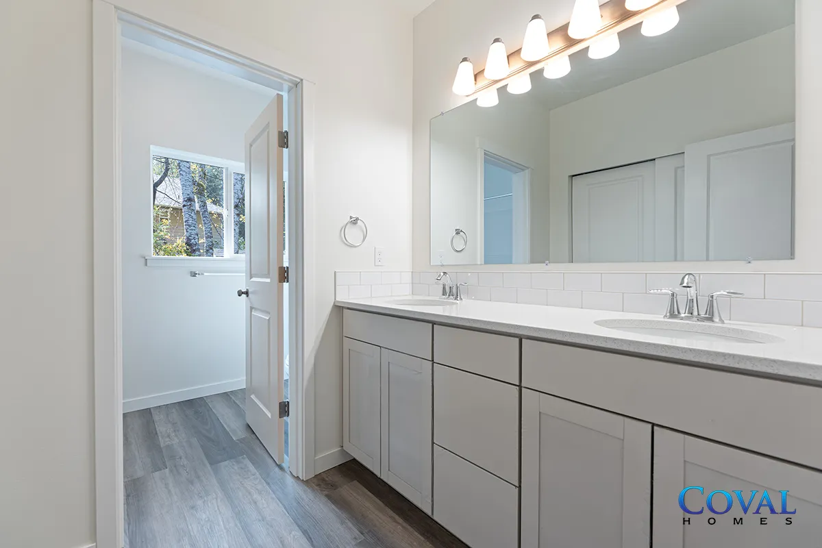 Bright bathroom with double sink vanity, large mirror, and doorway to a tiled shower area