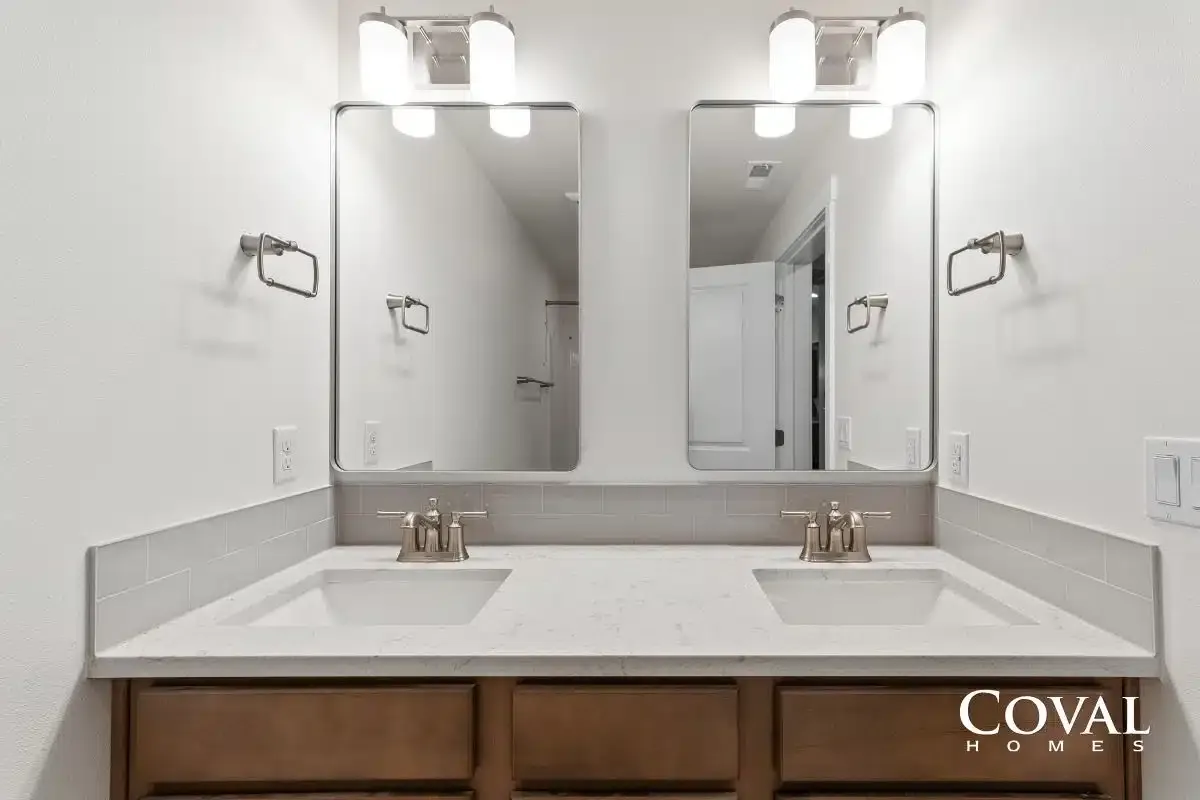 Double vanity bathroom with large mirrors, white countertops, and wall sconces