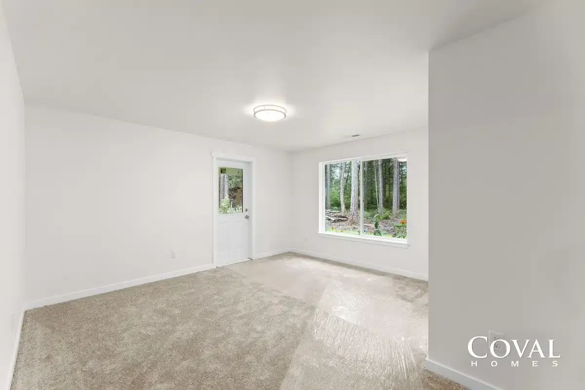 Empty white room with beige carpet, ceiling light, and a window overlooking trees