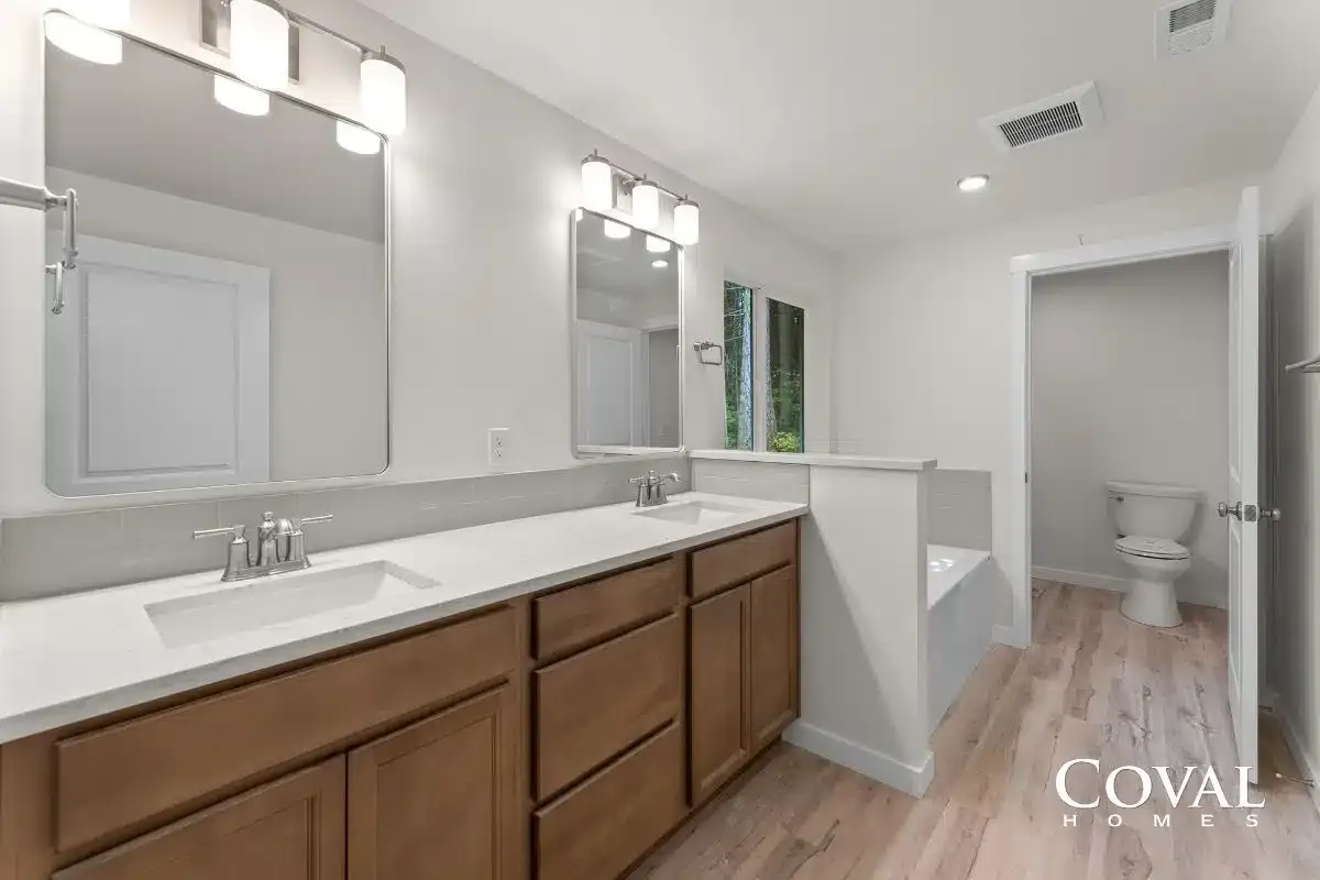 Modern bathroom with double vanity, wood cabinets, large mirror, and adjoining toilet room