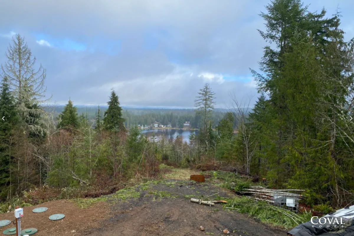 Wooded hillside clearing overlooking a distant town under a cloudy blue sky