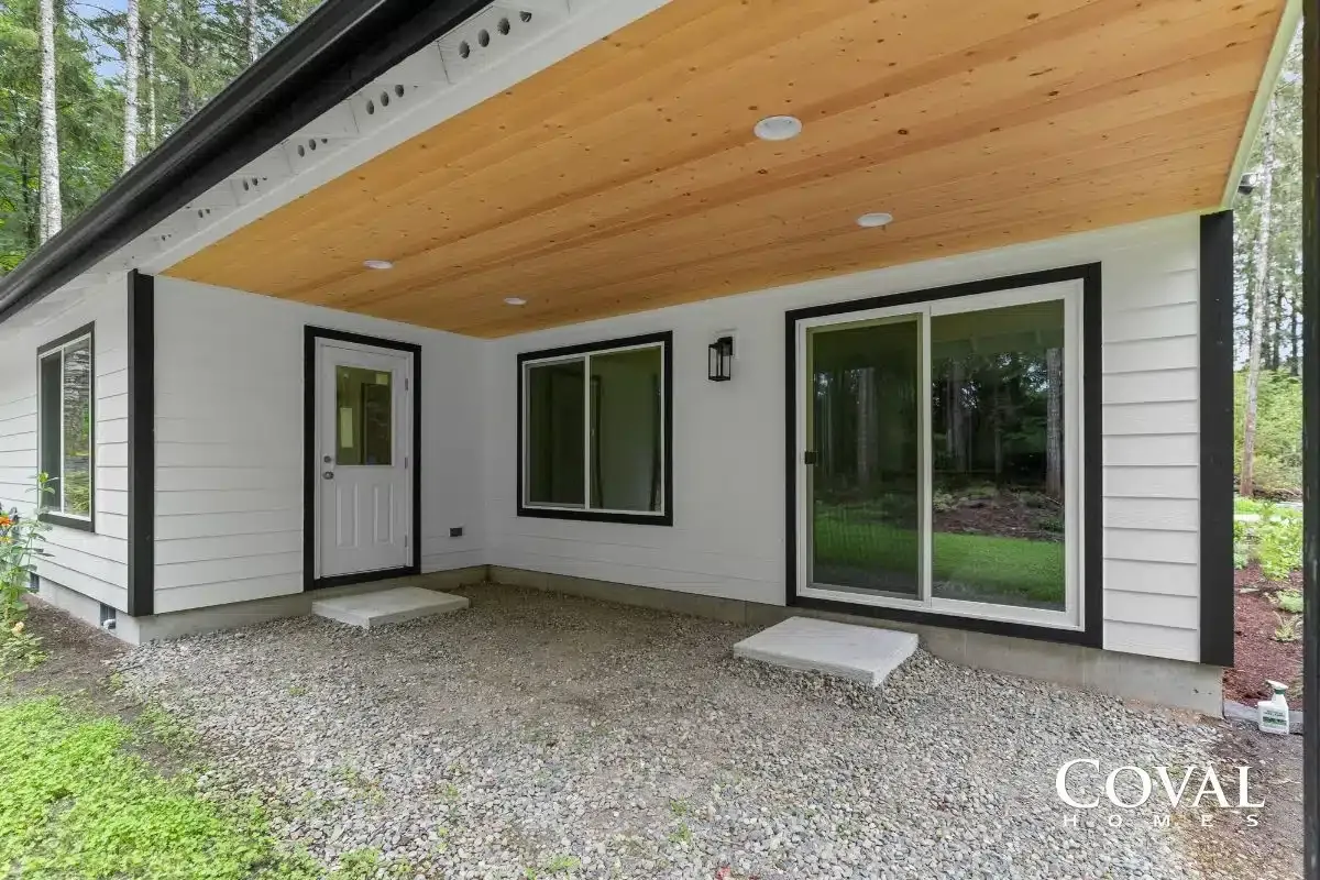 Modern house exterior with wood soffit, white siding, sliding glass door, and covered gravel patio