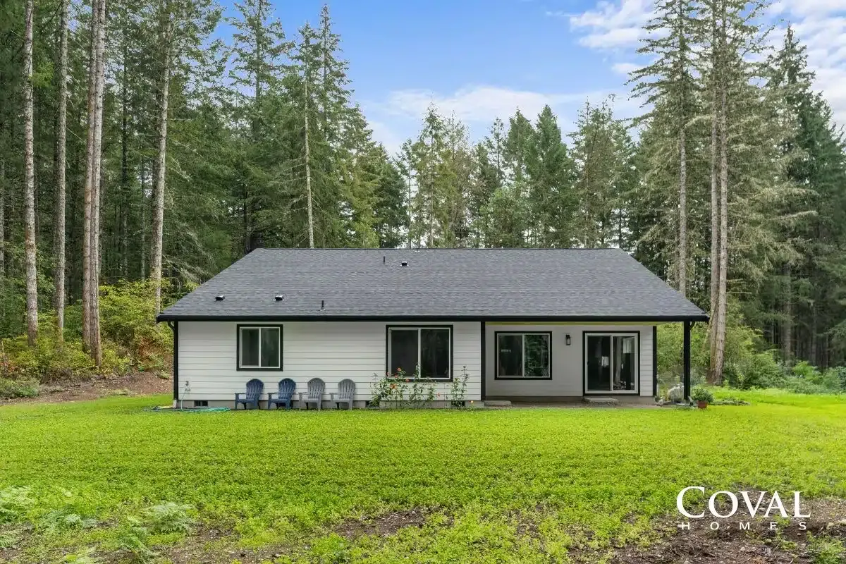 Modern single-story white house with dark roof in a forest clearing surrounded by tall trees