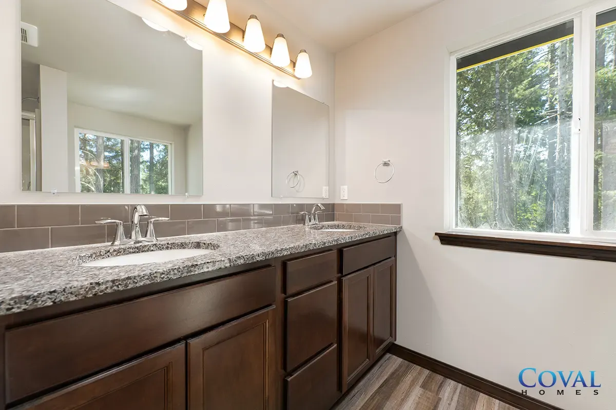 Modern bathroom with dark wood vanity, speckled countertop, large mirror, and bright window light