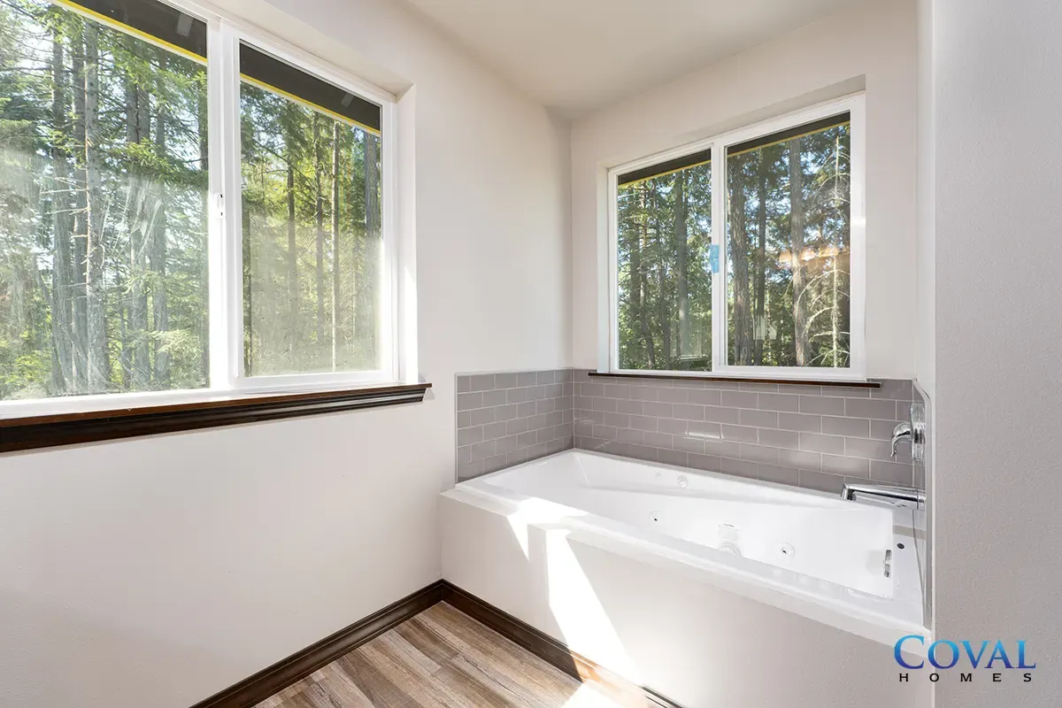 Bright bathroom with large windows, white tub, and gray tile accent wall overlooking trees