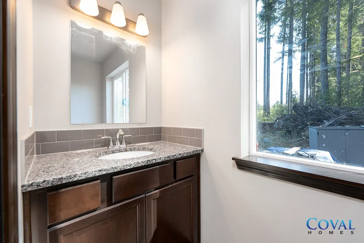 Bathroom vanity with granite countertop, mirror, and a large window overlooking trees