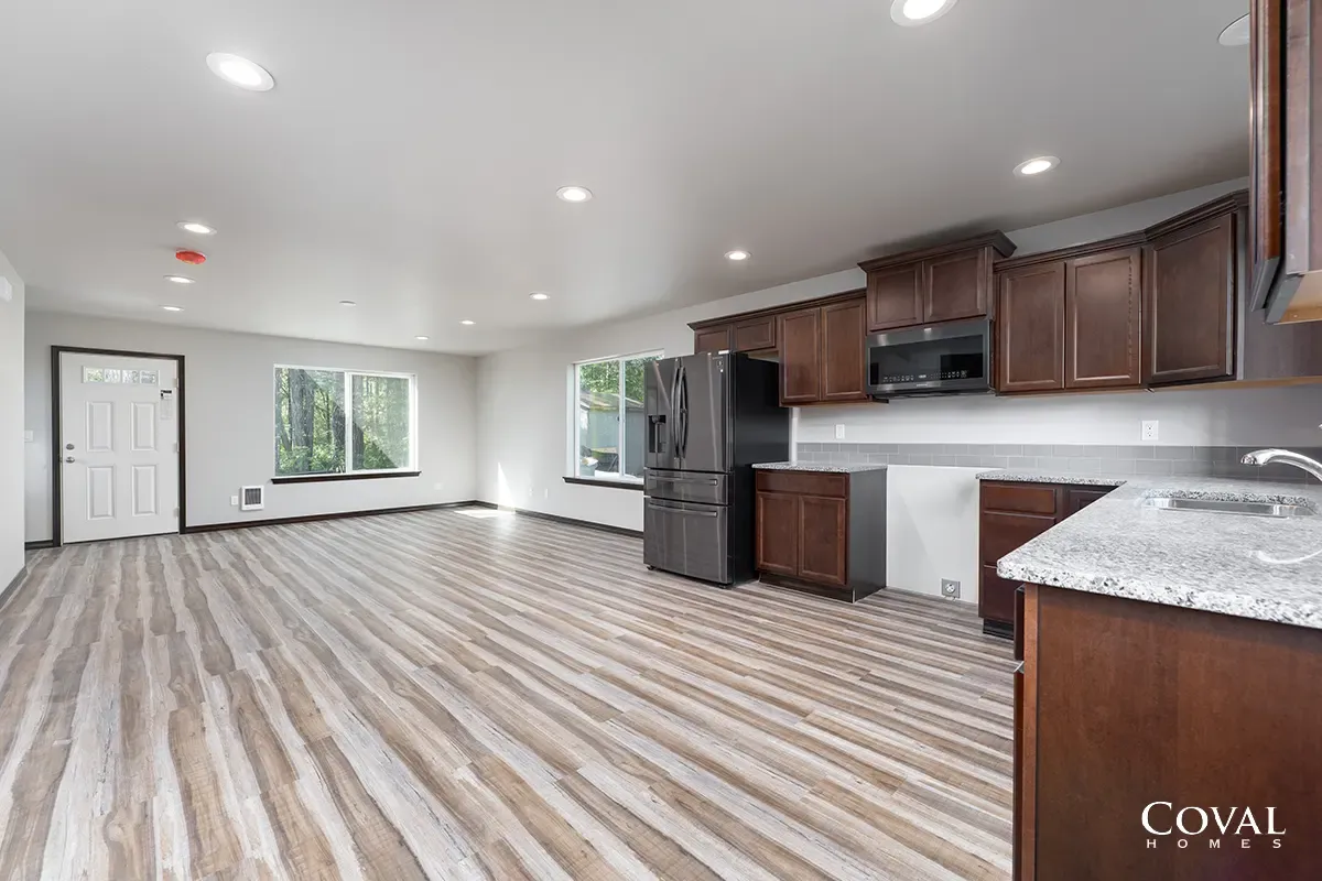 Empty open-plan kitchen and living area with dark wood cabinets, black appliances, and light striped flooring.