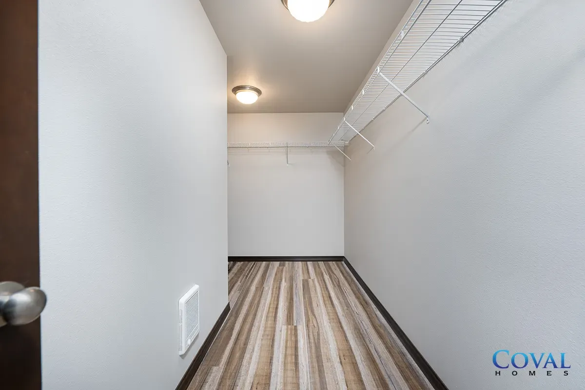 Narrow empty walk-in closet with striped carpet, white walls, wire shelves, and ceiling lights