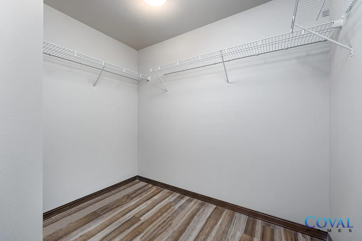 Empty walk-in closet with white walls, wire shelves, and striped wood flooring.