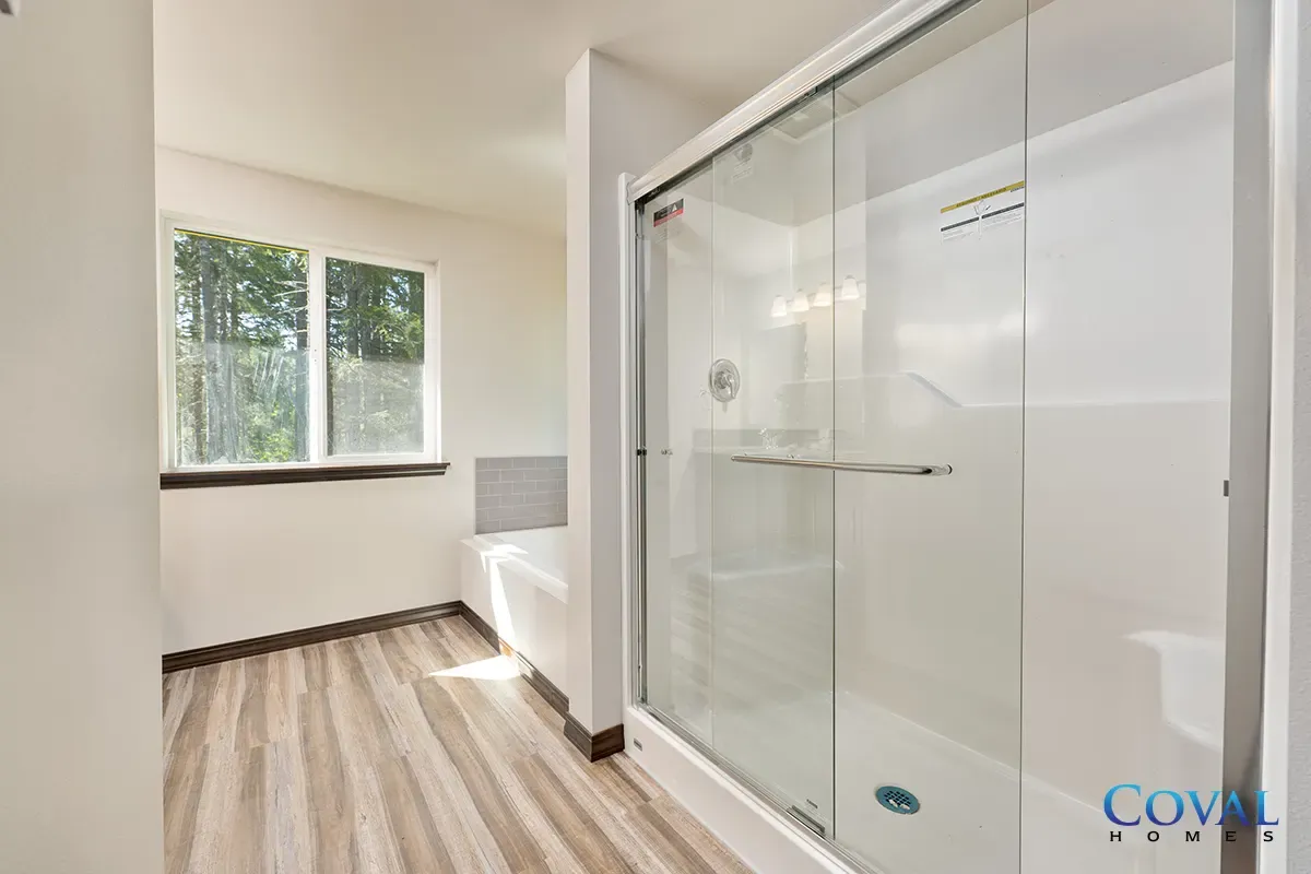 Bright bathroom with glass shower, window light, and wood-look flooring