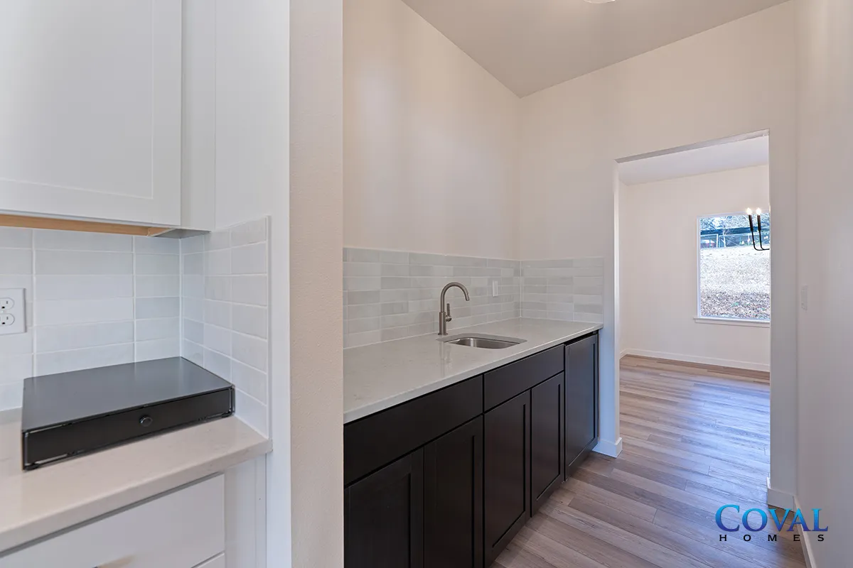 Bright kitchen with white cabinets, dark countertops, and a windowed doorway to a sunlit room