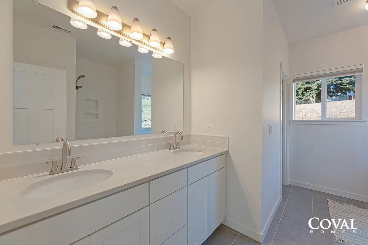 Bright white bathroom with double vanity, large mirror, and small window
