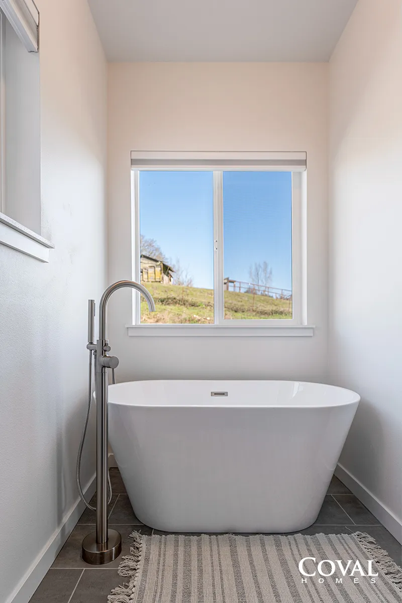 Small modern bathroom with a freestanding white tub, chrome floor faucet, and window above.
