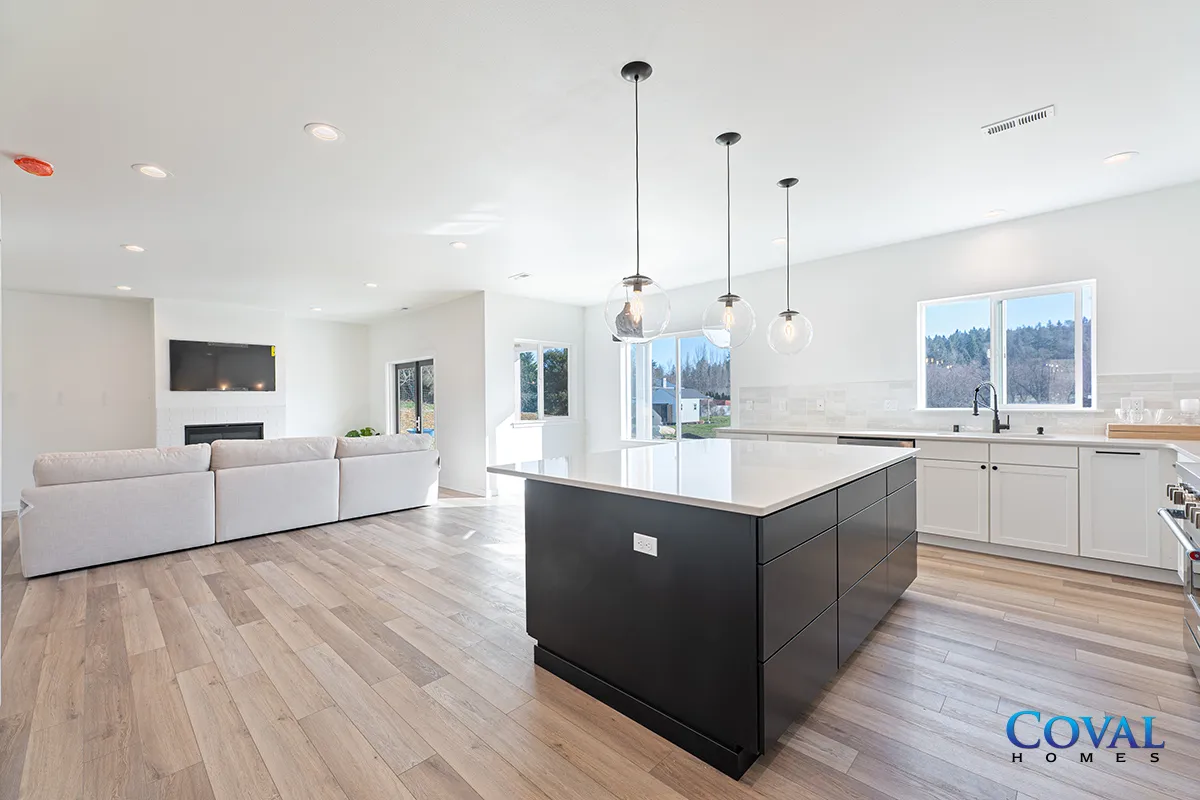 Bright modern kitchen and living room with island, white cabinets, light wood floors, and large windows.