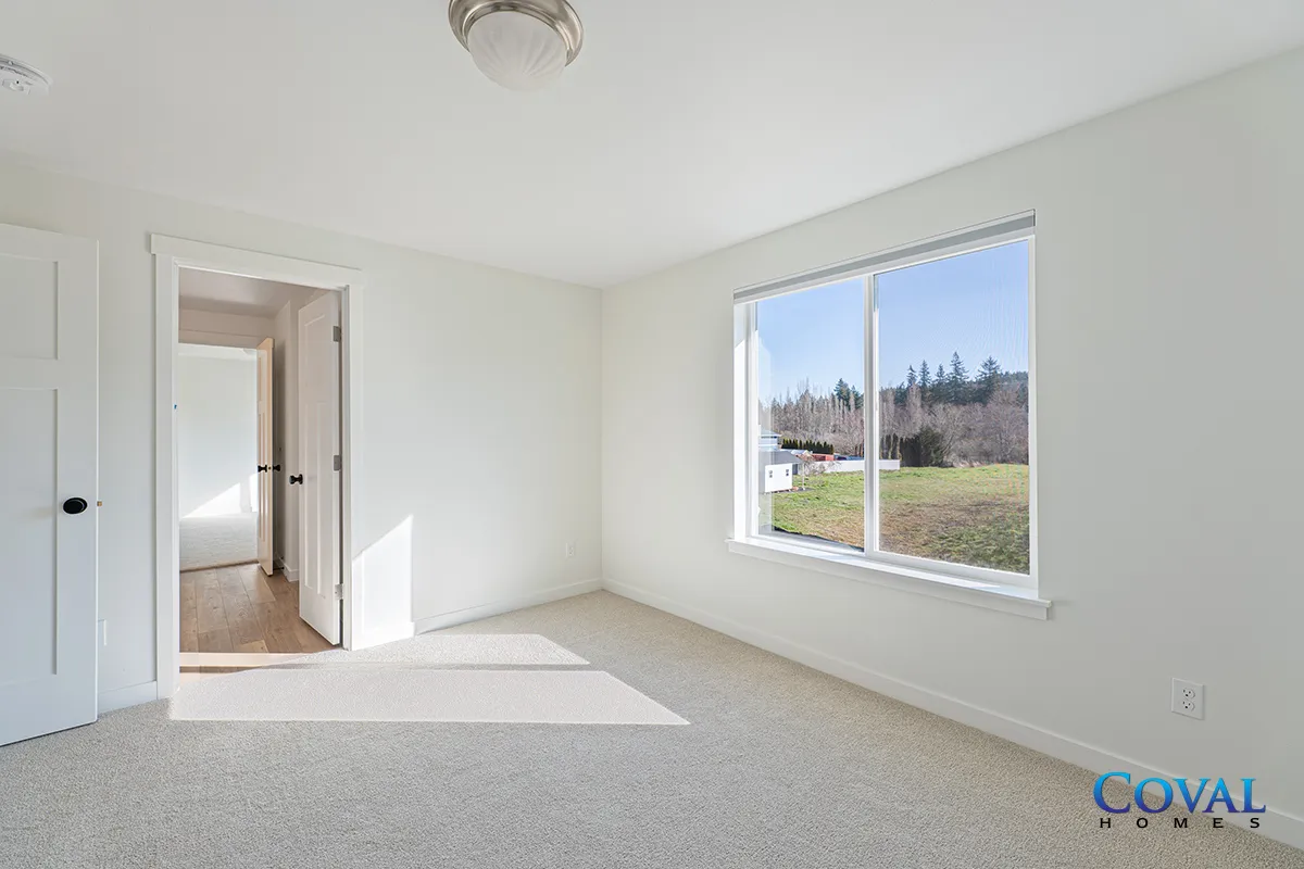 Empty white bedroom with carpet, open doorway, and large window overlooking a grassy yard