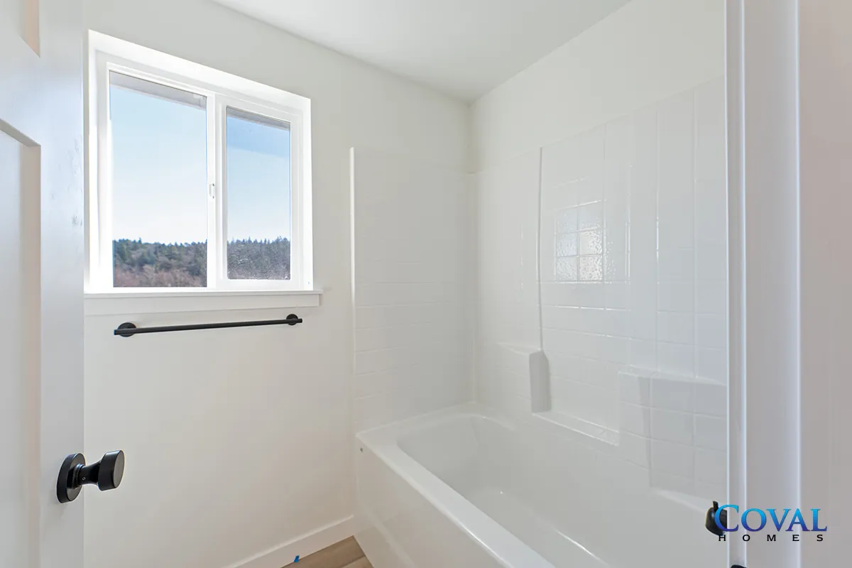 Bright white bathroom with a bathtub, window, and black towel bar.