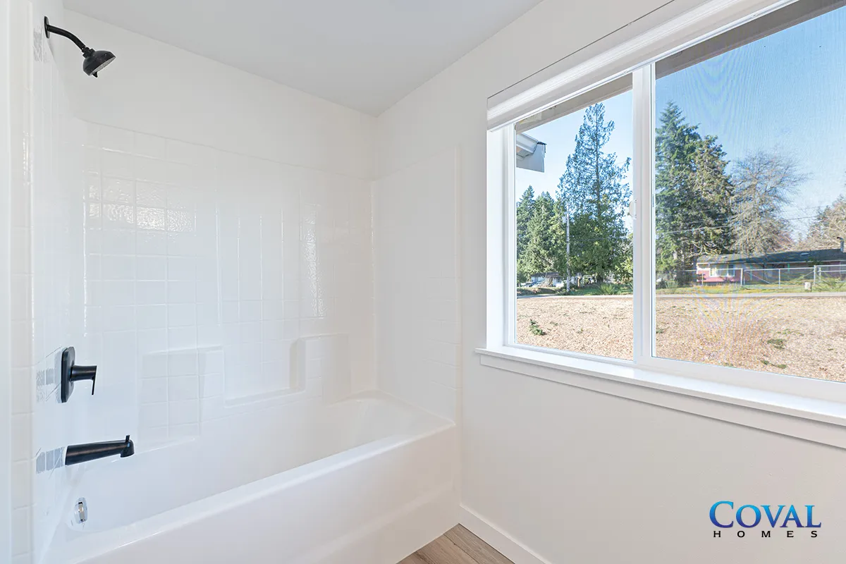 Bright white bathroom with a shower-tub combo and large window overlooking trees
