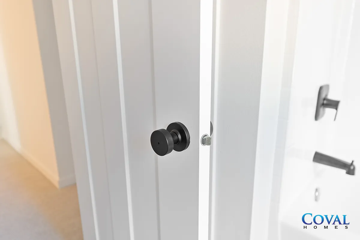 White interior door with black knob and silver latch in a hallway, slightly ajar