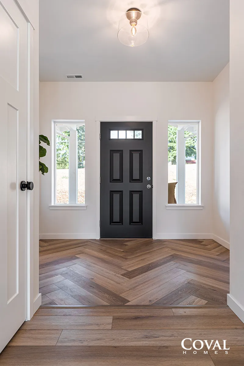 Bright entryway with black front door, white walls, and wood herringbone floor.