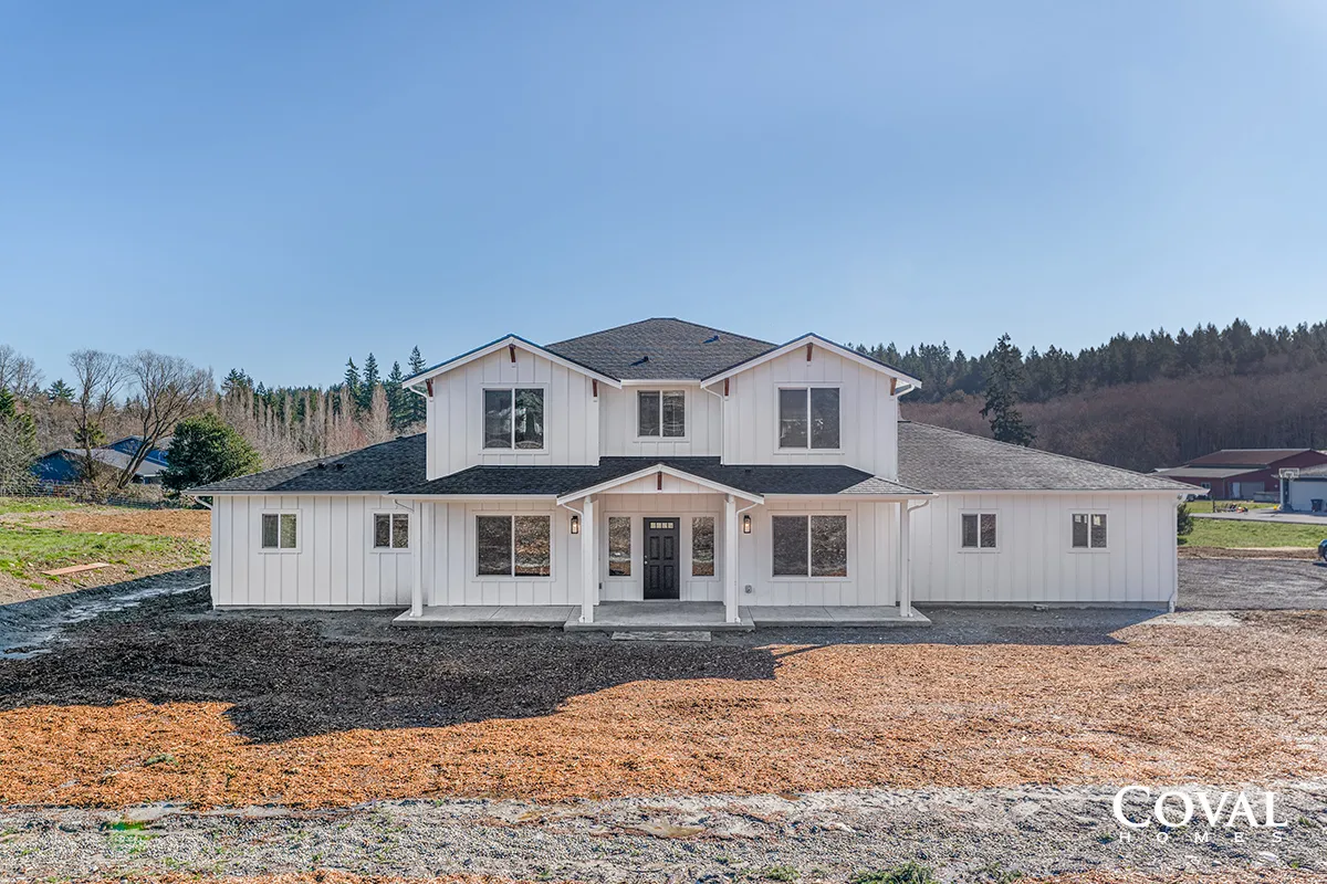 Two-story white house with dark roof and covered porch on a bare lot under a blue sky